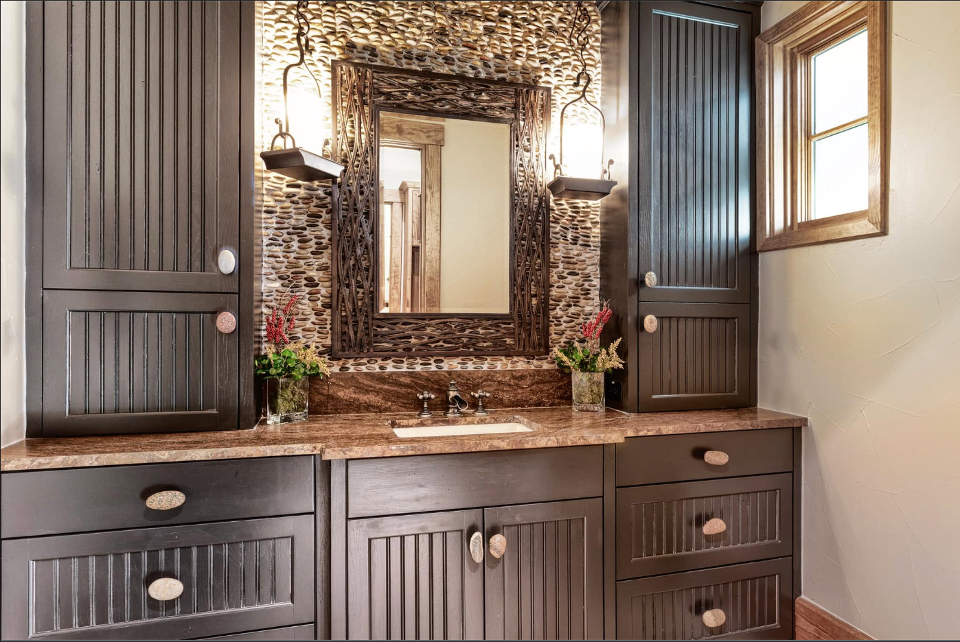 Dark custom vanity with river-stone wall and carved mirror